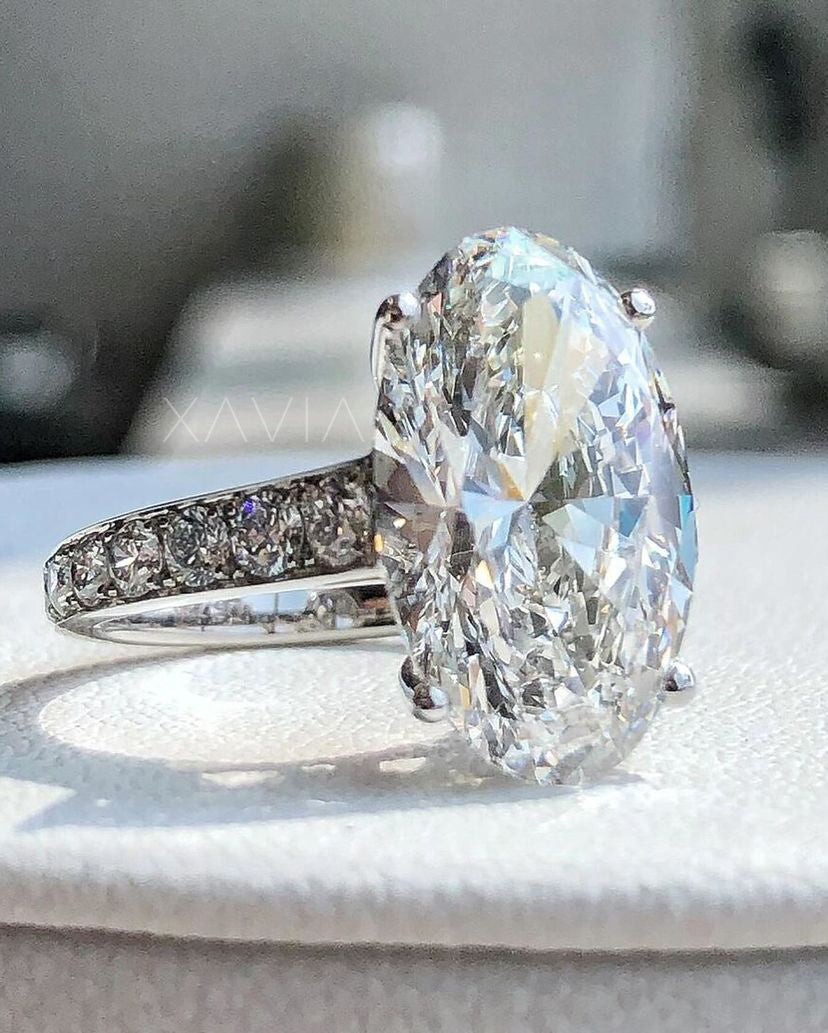 Angled close-up of oval cut lab diamond solitaire with pavé diamond shank in high-polish platinum finish